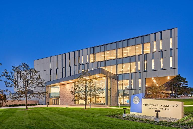 An exterior view of the Learning Commons at dusk with the lights on in the building.